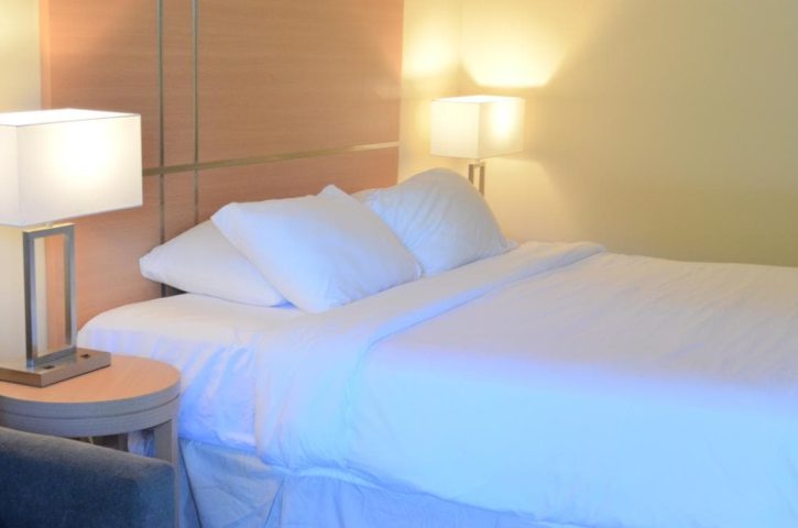 A tidy hotel room with a large bed, white linens, flanked by two nightstands and lit table lamps, creating a warm, inviting atmosphere.